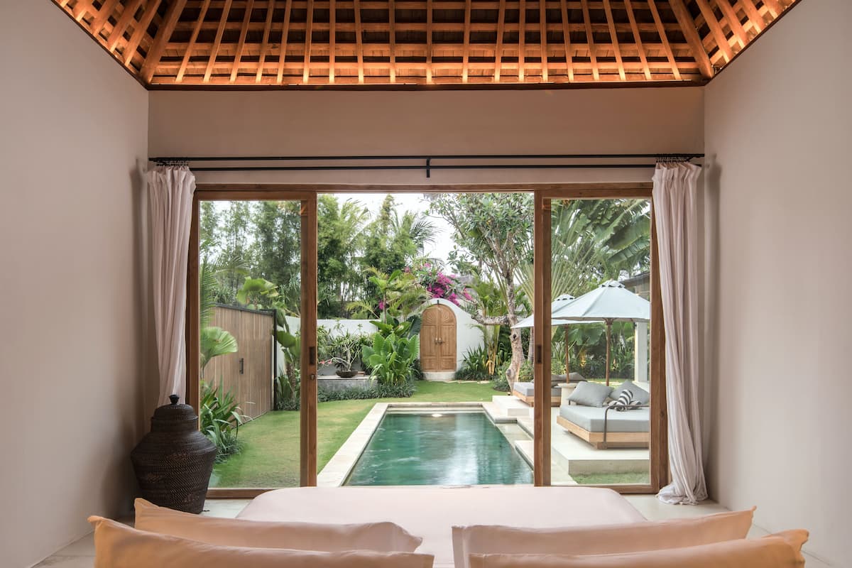 A bedroom with a large window, a bed, and a view of a swimming pool and garden.