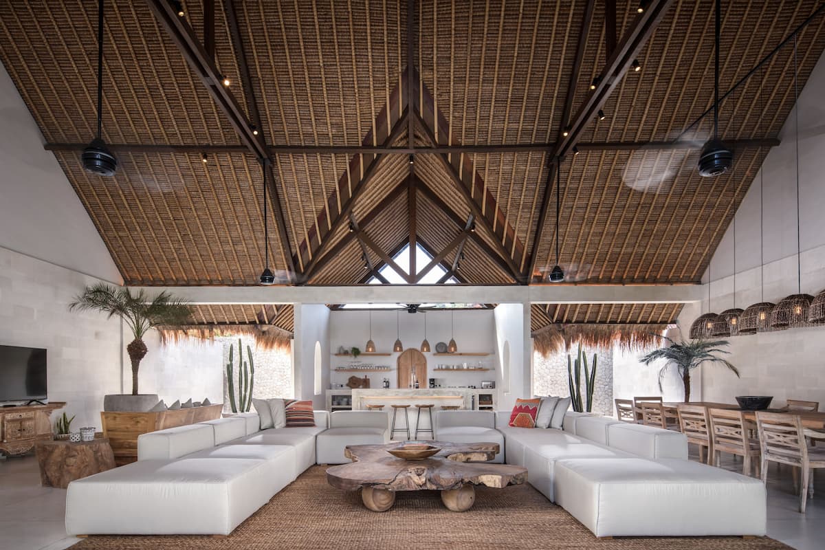 A spacious living area with a high ceiling, white sofas, a central coffee table, and a kitchen in the background.