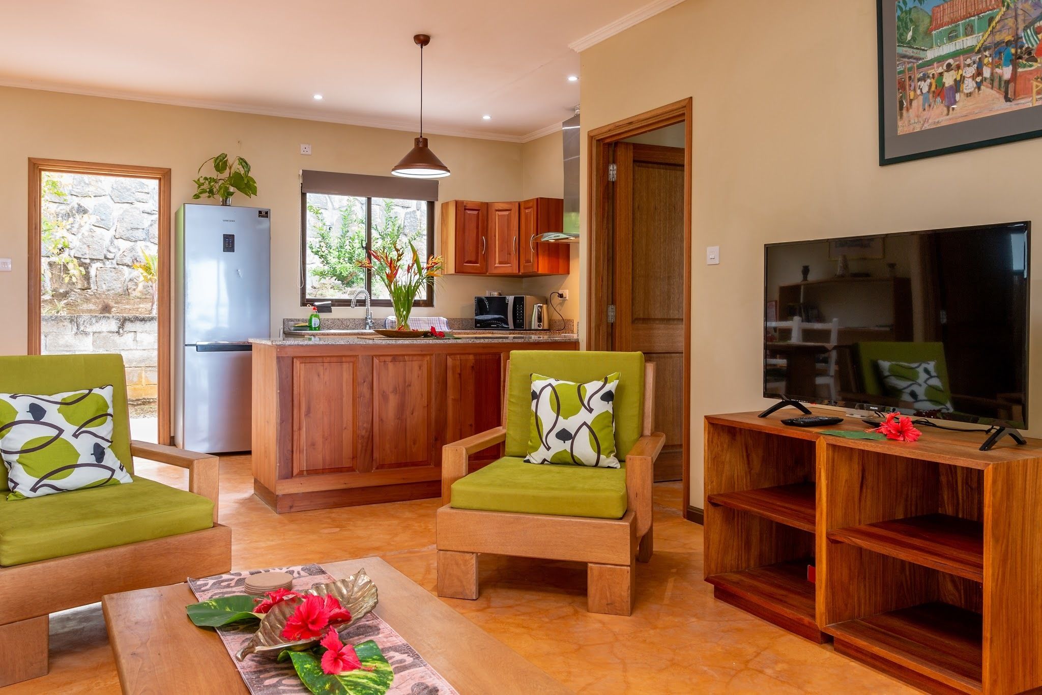 A modern kitchen with wooden cabinets, a refrigerator, and a dining area with green chairs and a coffee table.