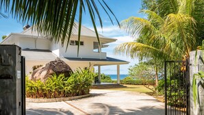 Una casa moderna con un portico coperto, un grande masso e vista sull'oceano.