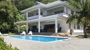 Una casa a due piani con piscina, facciata bianca e patio coperto.