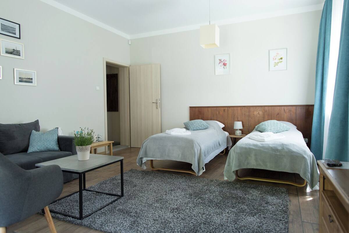 A modern, well-lit room with two single beds, a sofa, a small table, and a potted plant.