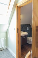 Un baño pequeño y moderno con puerta de madera, lavabo blanco e inodoro.