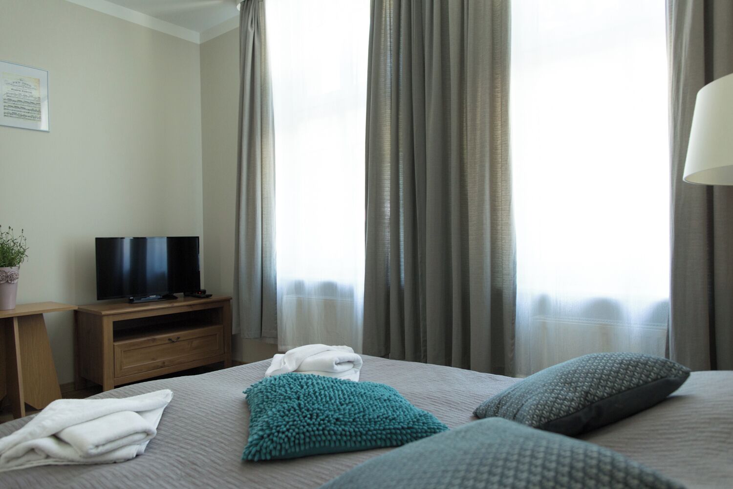 Ein Hotelzimmer mit einem Bett, einem Fernseher auf einem Holztischchen, einer Zimmerpflanze und einem Fenster mit Vorhängen.