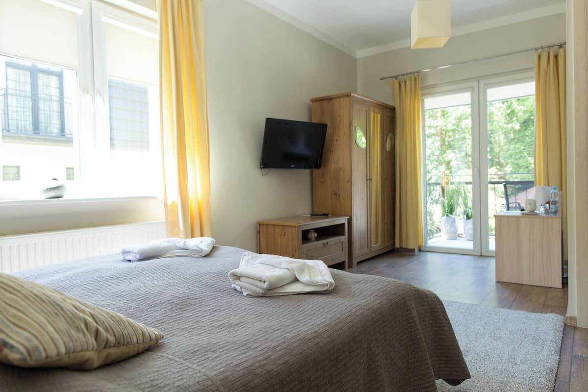 A hotel room with a bed, a TV, a wooden cabinet, and a balcony with curtains.