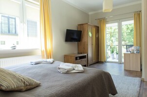 A hotel room with a bed, a TV, a wooden cabinet, and a balcony with curtains.