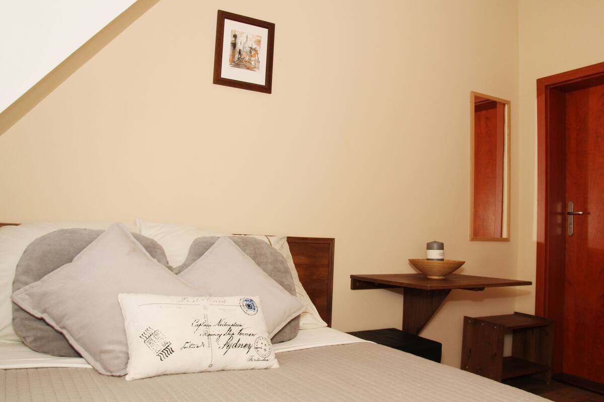 A neatly arranged bedroom with a bed, pillows, a small table with a bowl, and a framed picture on the wall.