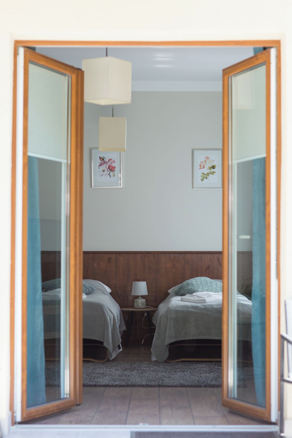 Ein Schlafzimmer mit zwei Betten, einem hölzernen Kopfteil, einem Nachttisch mit Lampe und gerahmten floralen Bildern an der Wand.