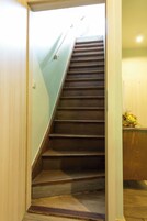 Un escalier en bois, doté d’une rampe, m ène à un palier recouvert de parquet et sur lequel se trouve une petite table ornée d’un vase de fleurs.