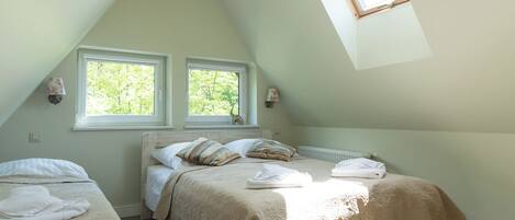Un dormitorio con dos camas, techo inclinado y dos ventanas.