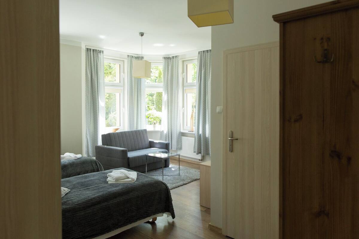 A room with two beds, a sofa, and a window with curtains.