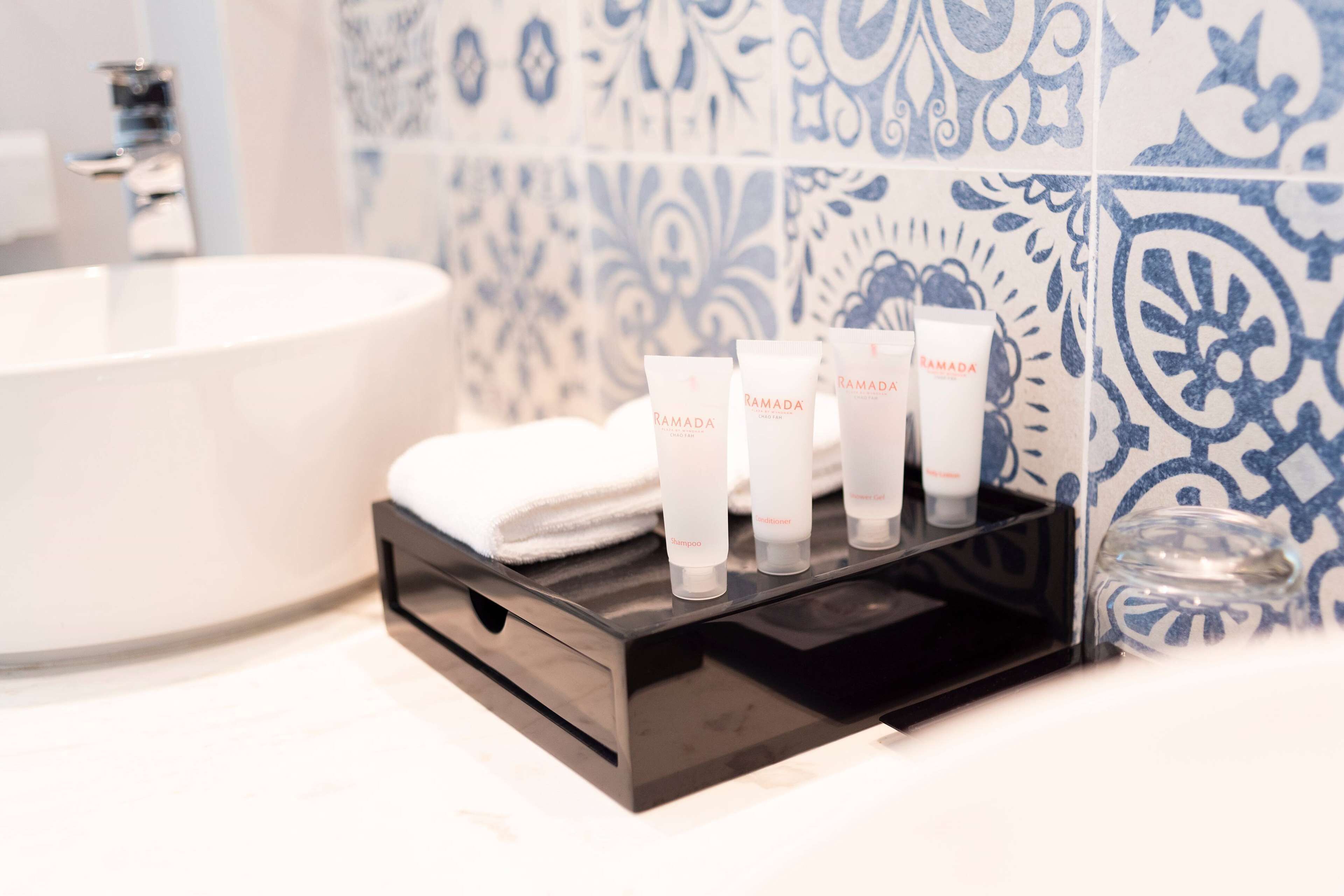 A bathroom with a white bathtub, a black tray holding three toiletries, and a patterned tile wall.
