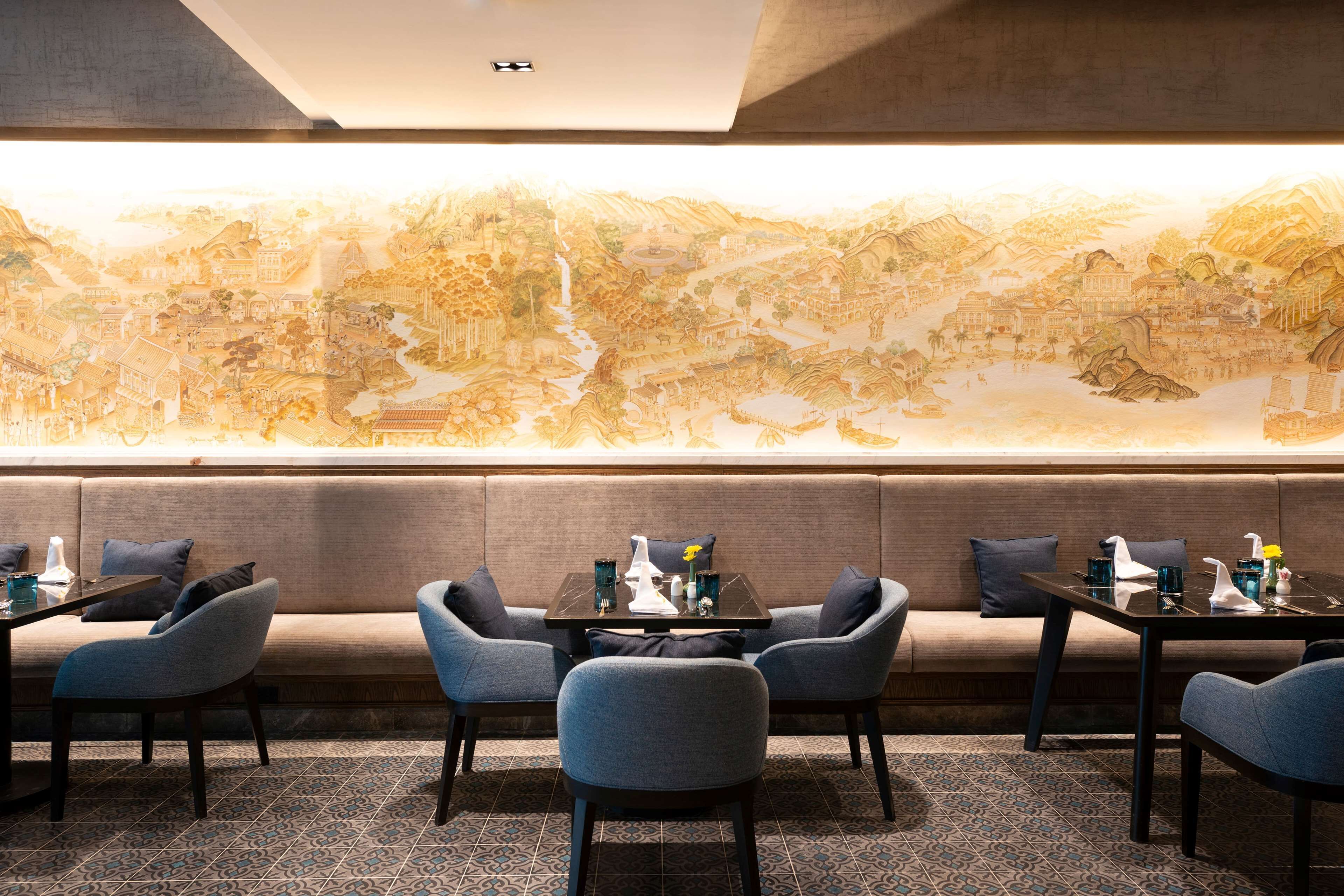 Un restaurante con un gran mural, asientos a lo largo de la pared y una mesa preparada con vasos y cubiertos.
