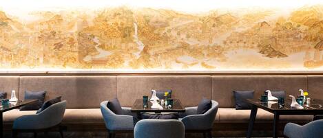 Un restaurante con un gran mural, asientos a lo largo de la pared y una mesa preparada con vasos y cubiertos.