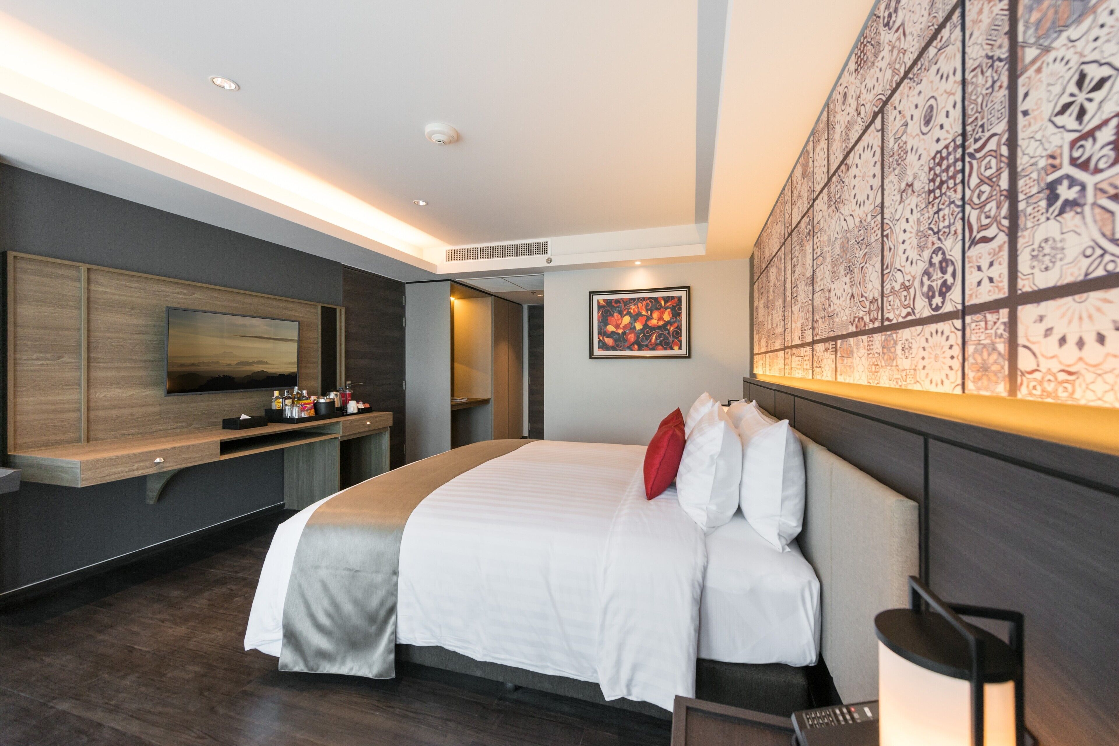 Una habitación de hotel moderna con una cama grande, un televisor de pantalla plana en la pared, un minibar y un panel decorativo.