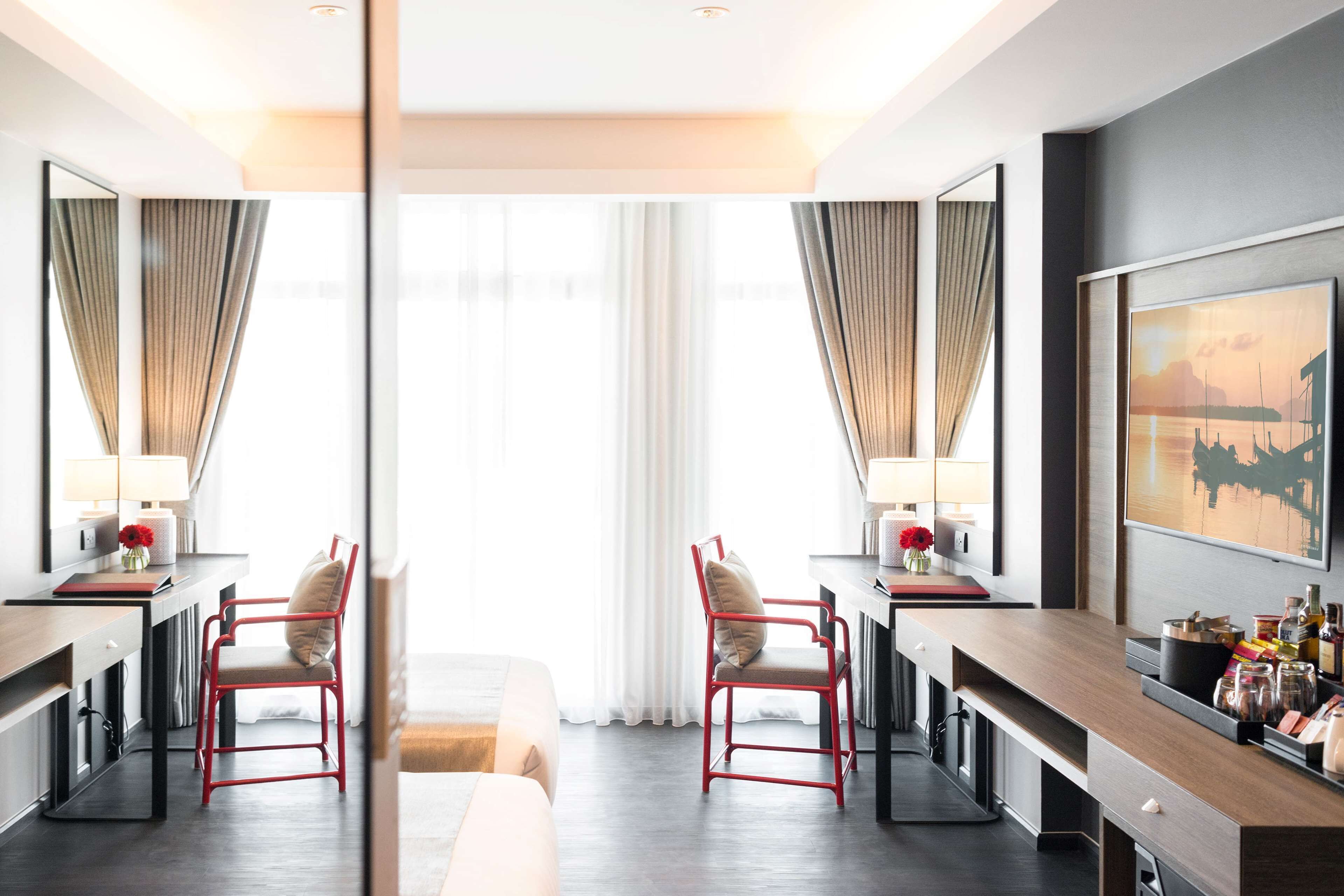 Une chambre d’hôtel moderne, dotée d’un grand lit, d’un bureau avec une chaise, d’un miroir et d’un tableau au mur.