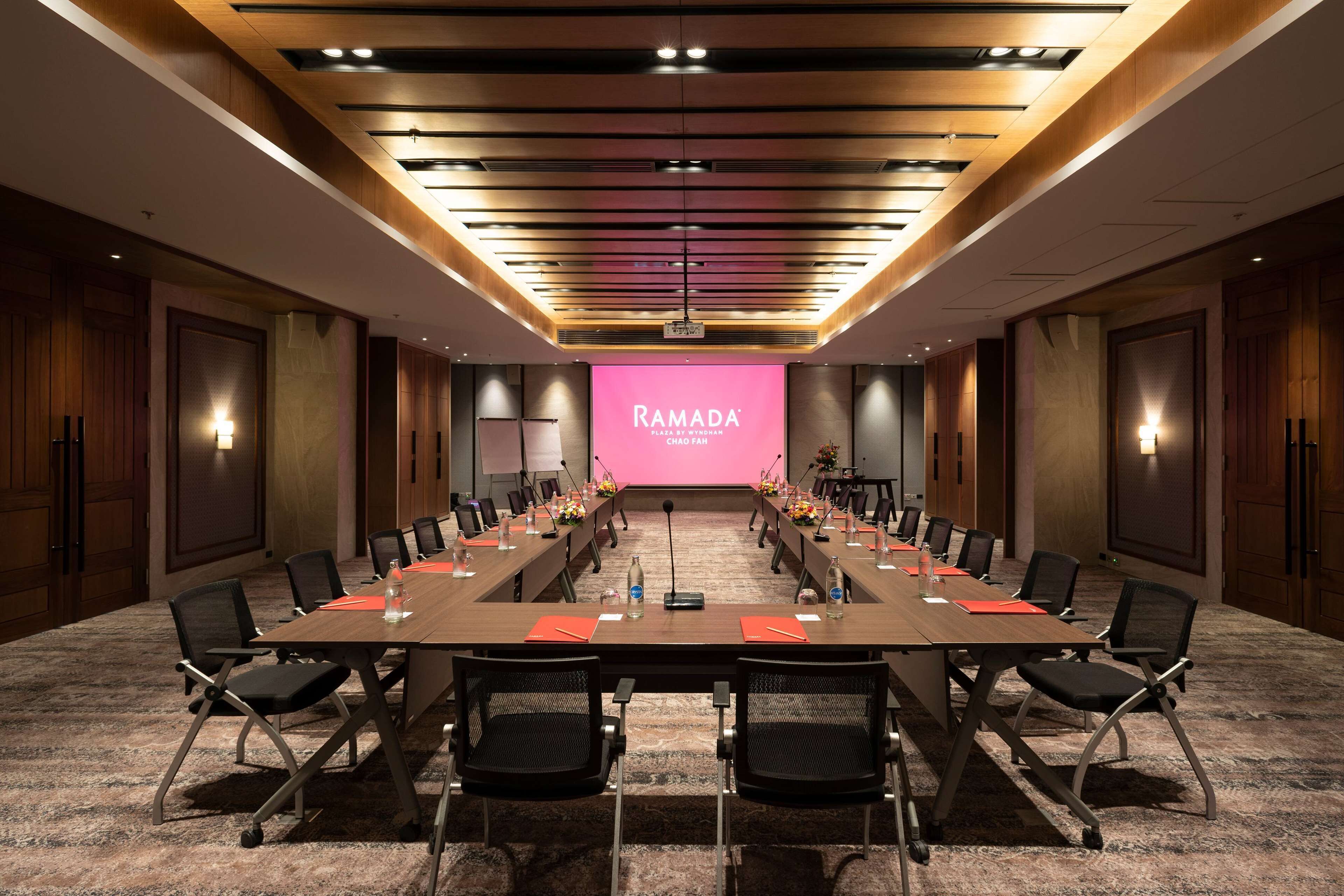 A conference room with a long table, chairs, a podium, and a pink screen displaying "RAMADA".