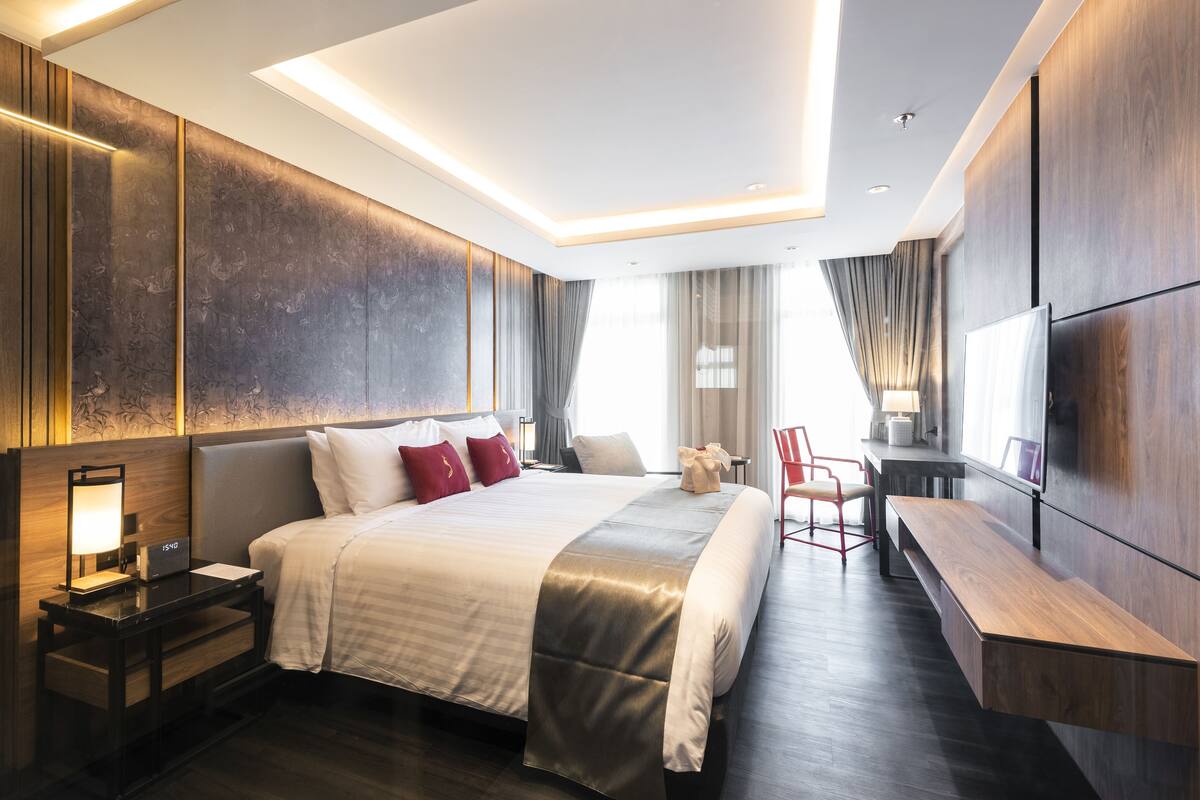 A modern hotel room with a large bed, bedside tables, a desk, and a TV.