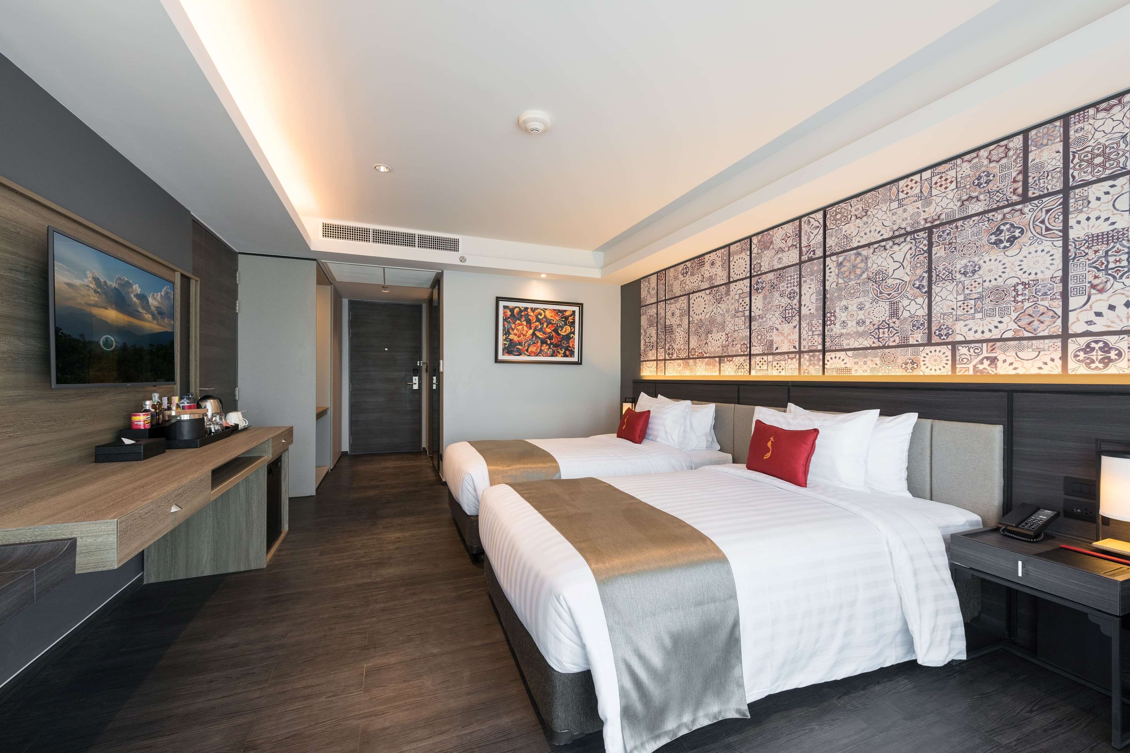 A modern hotel room with two beds, a desk, and a large decorative wall.