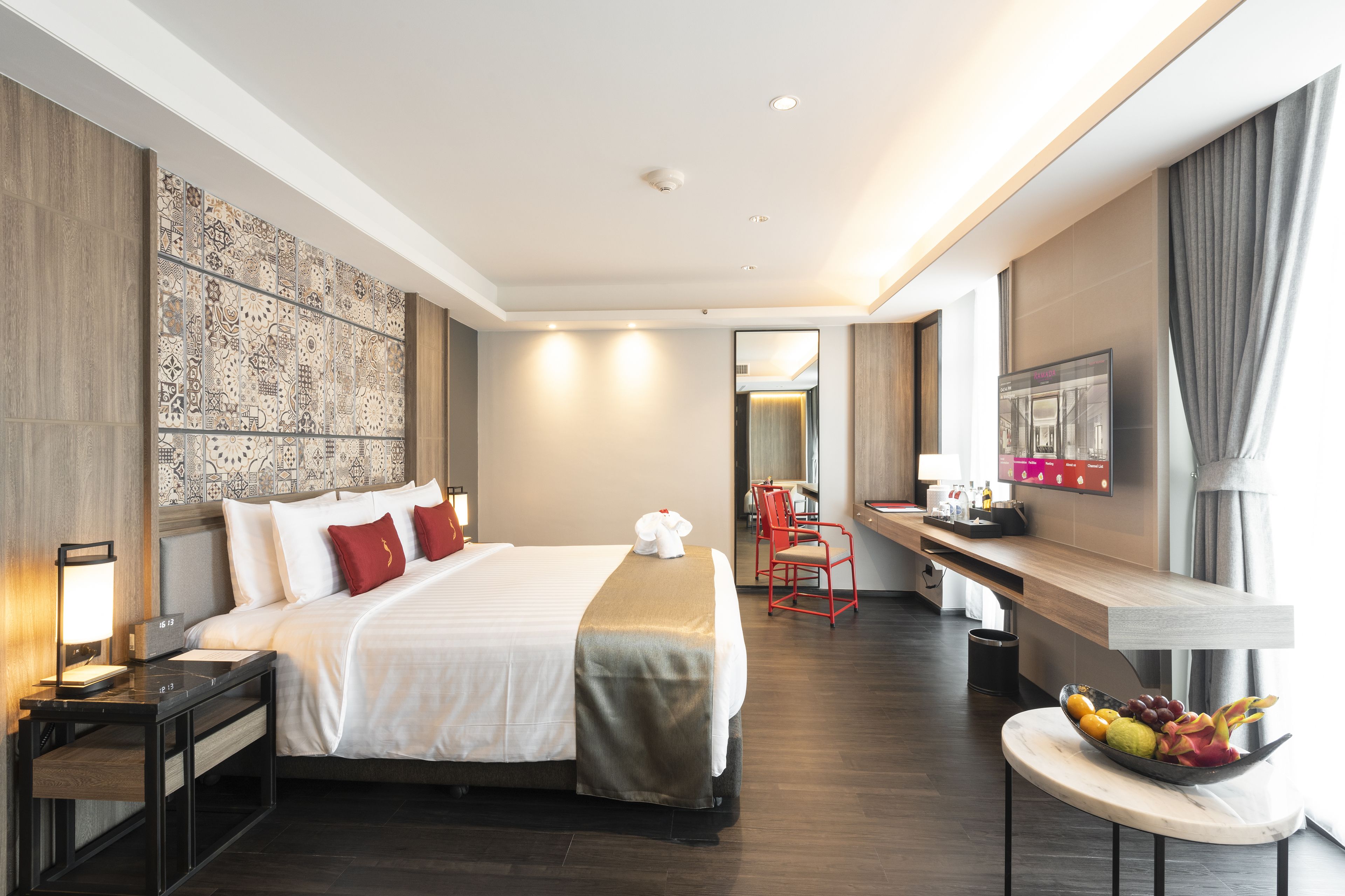 Habitación de hotel con una cama grande, un escritorio con silla, un frutero y un televisor en la pared.