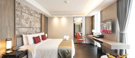 Habitación de hotel con una cama grande, un escritorio con silla, un frutero y un televisor en la pared.