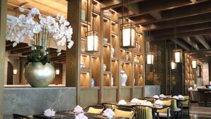 Un restaurant avec des tables dressées pour le service, un grand vase rempli de fleurs et des étagères ornées d’objets décoratifs.