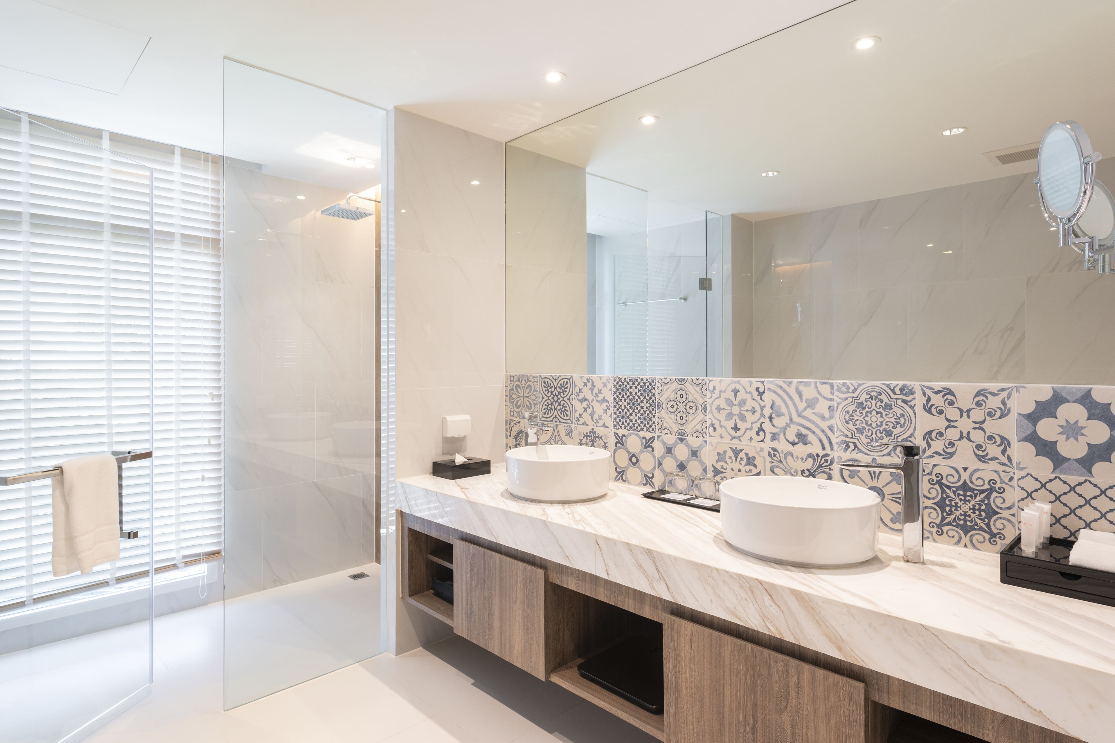 Un baño moderno con dos lavamanos, un espejo grande y un salpicadero de azulejos con diseño.
