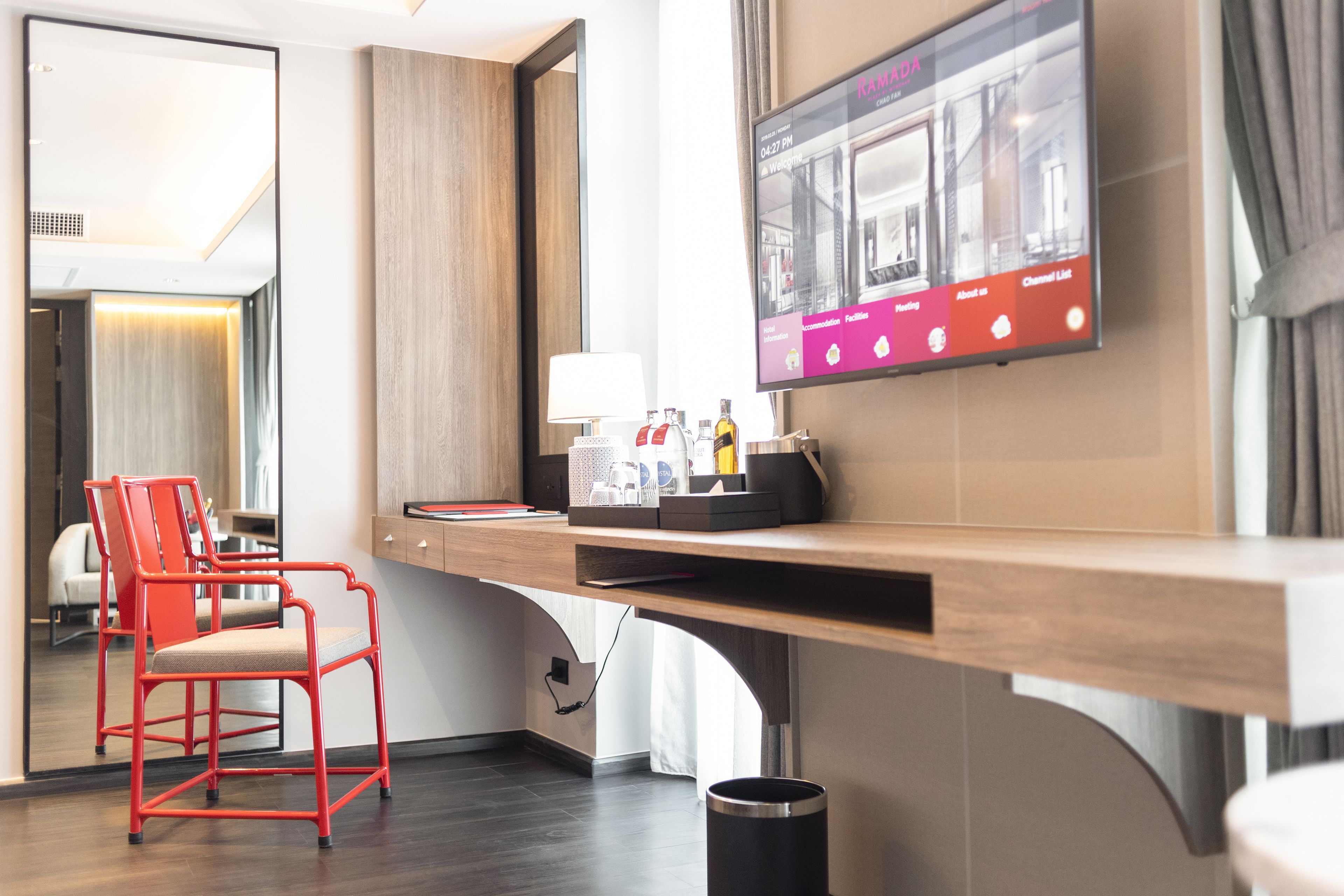 Une chambre d’hôtel avec un bureau en bois, une chaise rouge, un téléviseur fixé au mur et une poubelle.