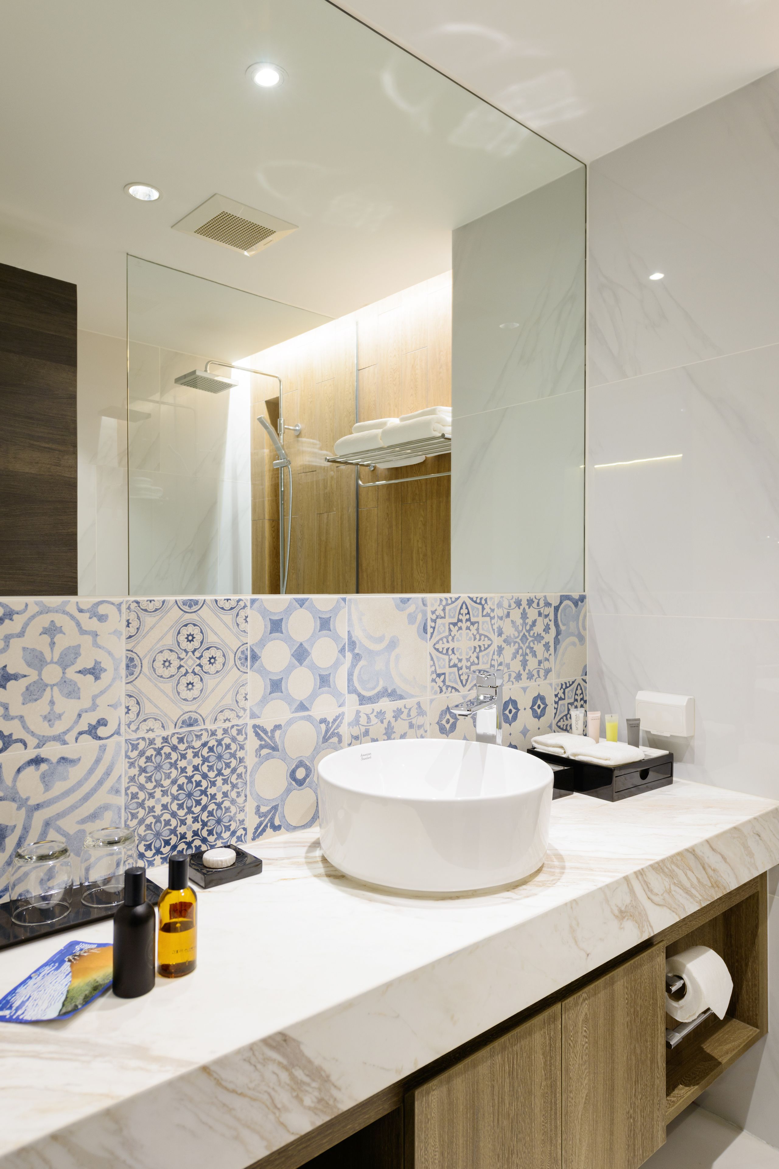 Une salle de bain moderne avec un grand miroir, un lavabo rond et des carreaux à motifs.