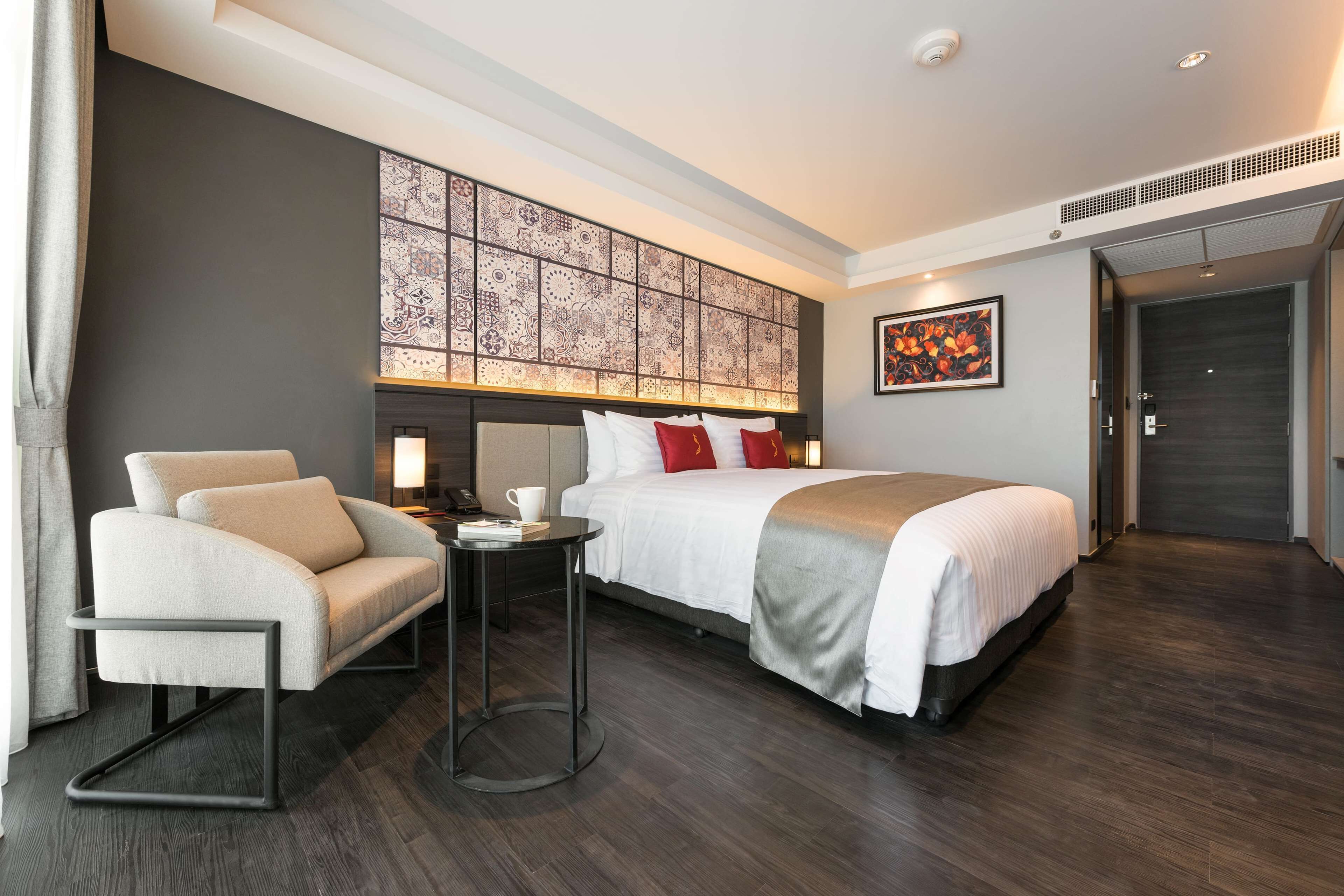 A modern hotel room with a large bed, a sofa, a small table, and a decorative wall panel.