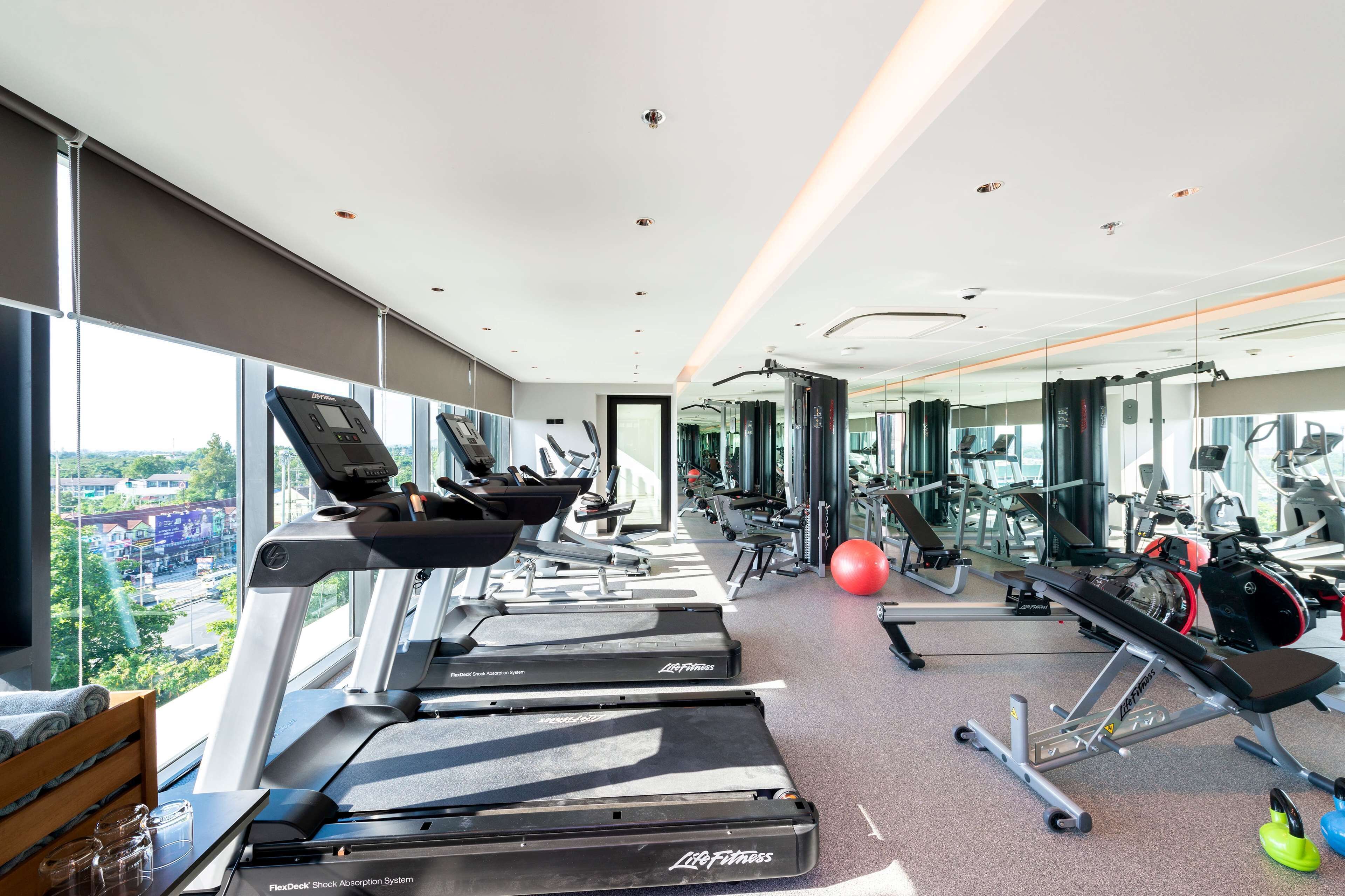 A modern gym with treadmills, weight machines, and a large window offering a city view.