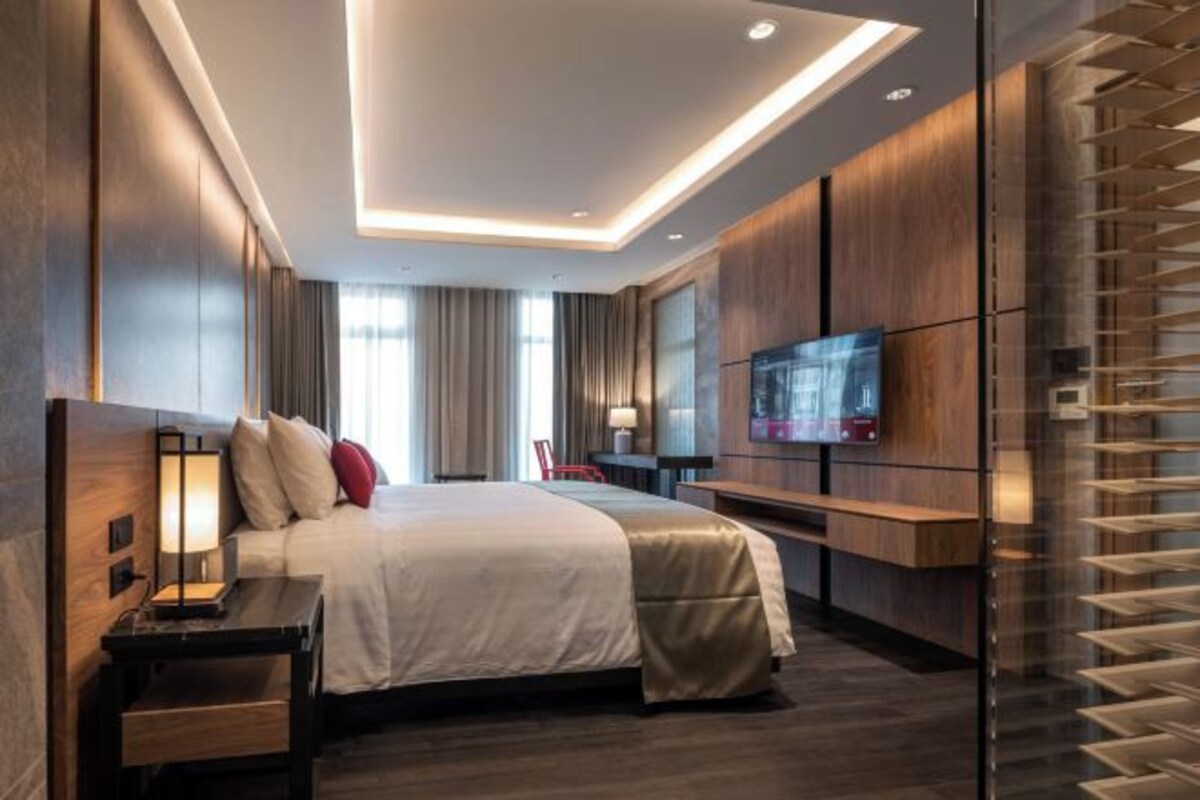 Een moderne hotelkamer met een bed, nachtkastje, televisie en een glazen scheiding.
