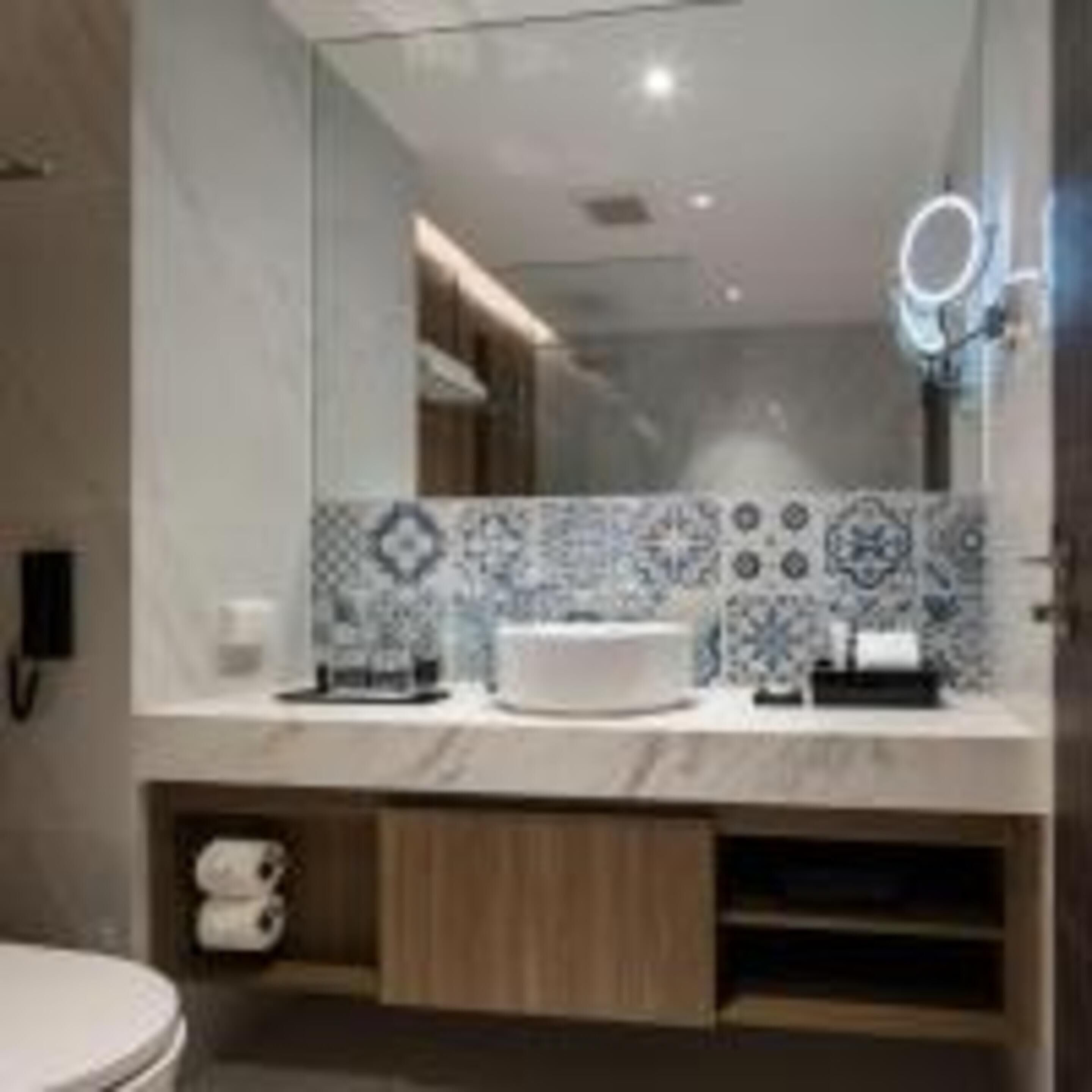 Un baño moderno con un espejo grande, un lavabo blanco y azulejos estampados.