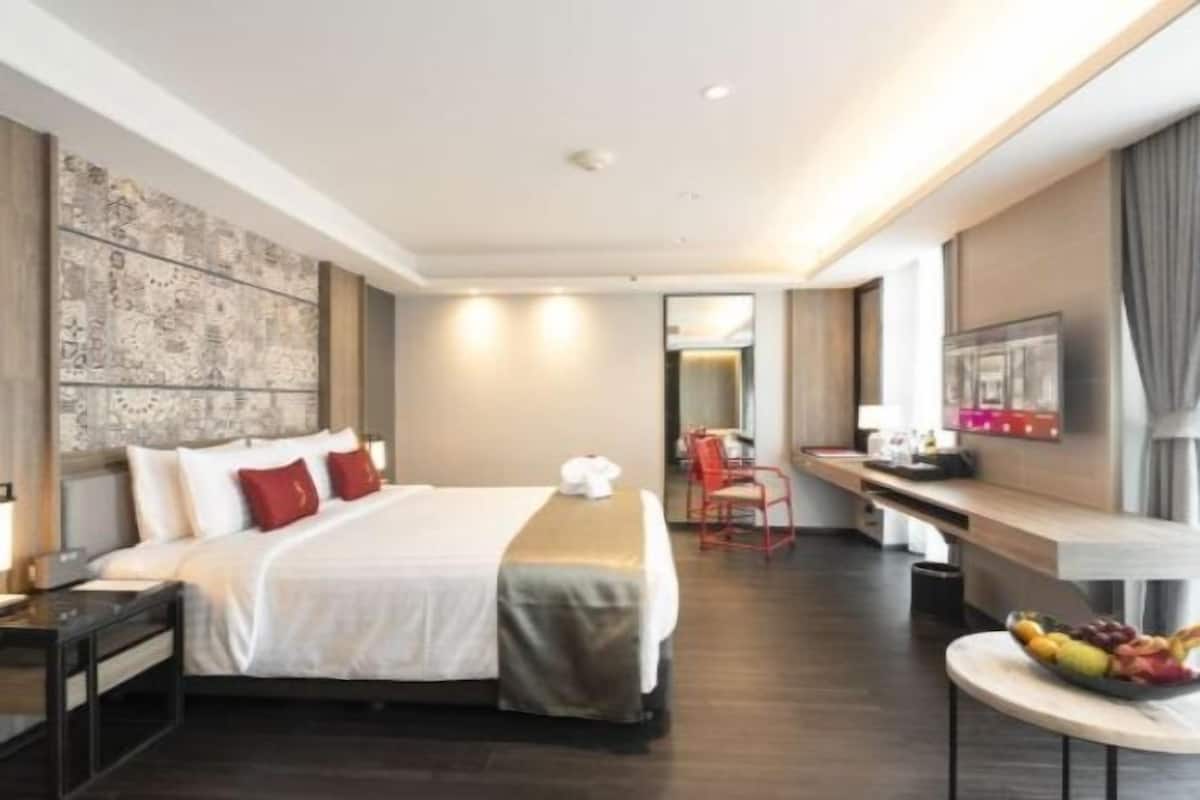 A hotel room with a bed, a desk, a chair, and a small table with fruit.