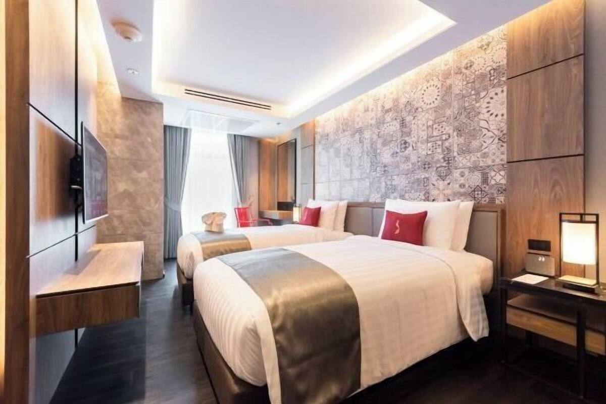 A modern hotel room with a large bed, bedside tables, a TV, and a patterned wall.