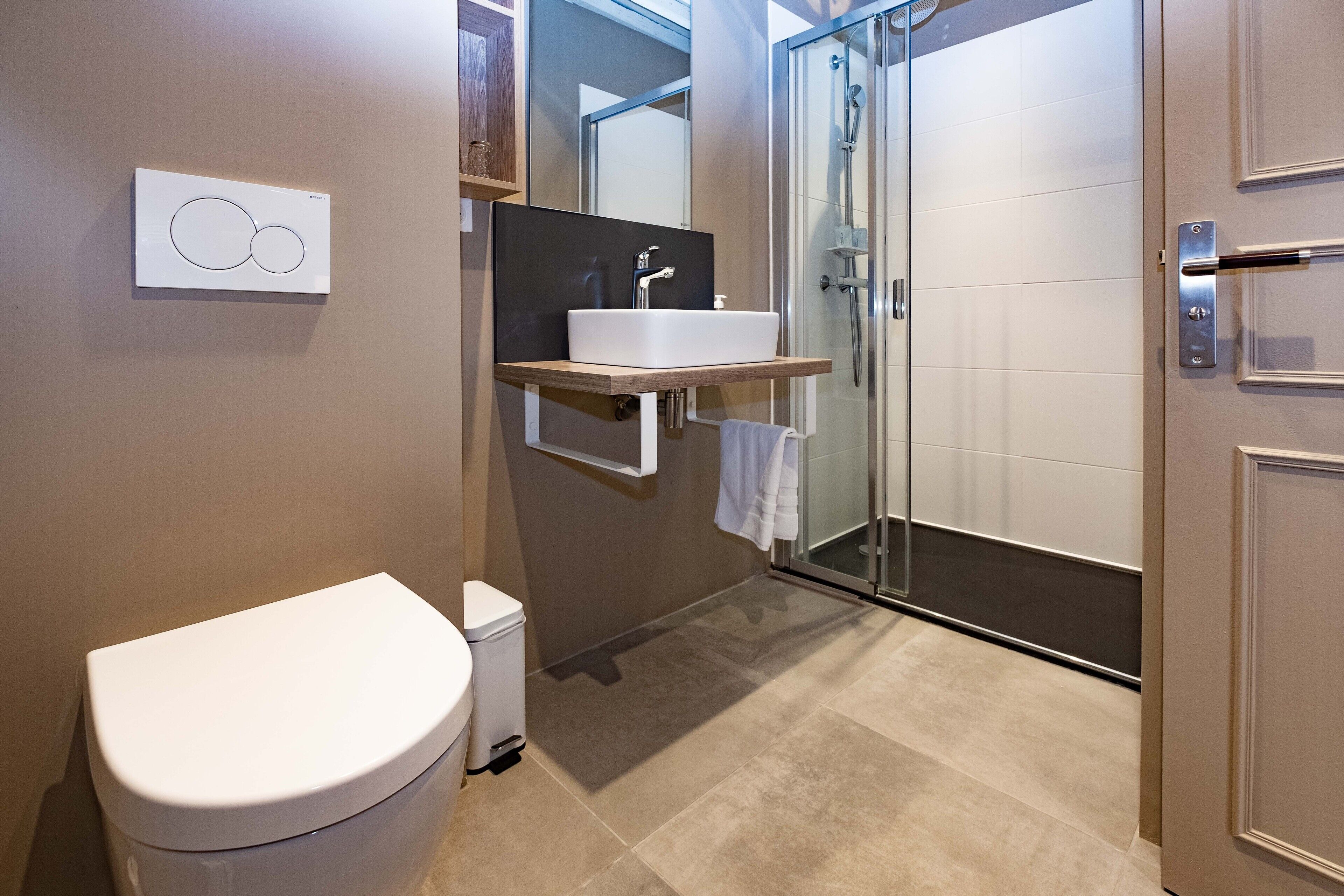 Un baño moderno con inodoro, lavamanos y cabina de ducha de vidrio.