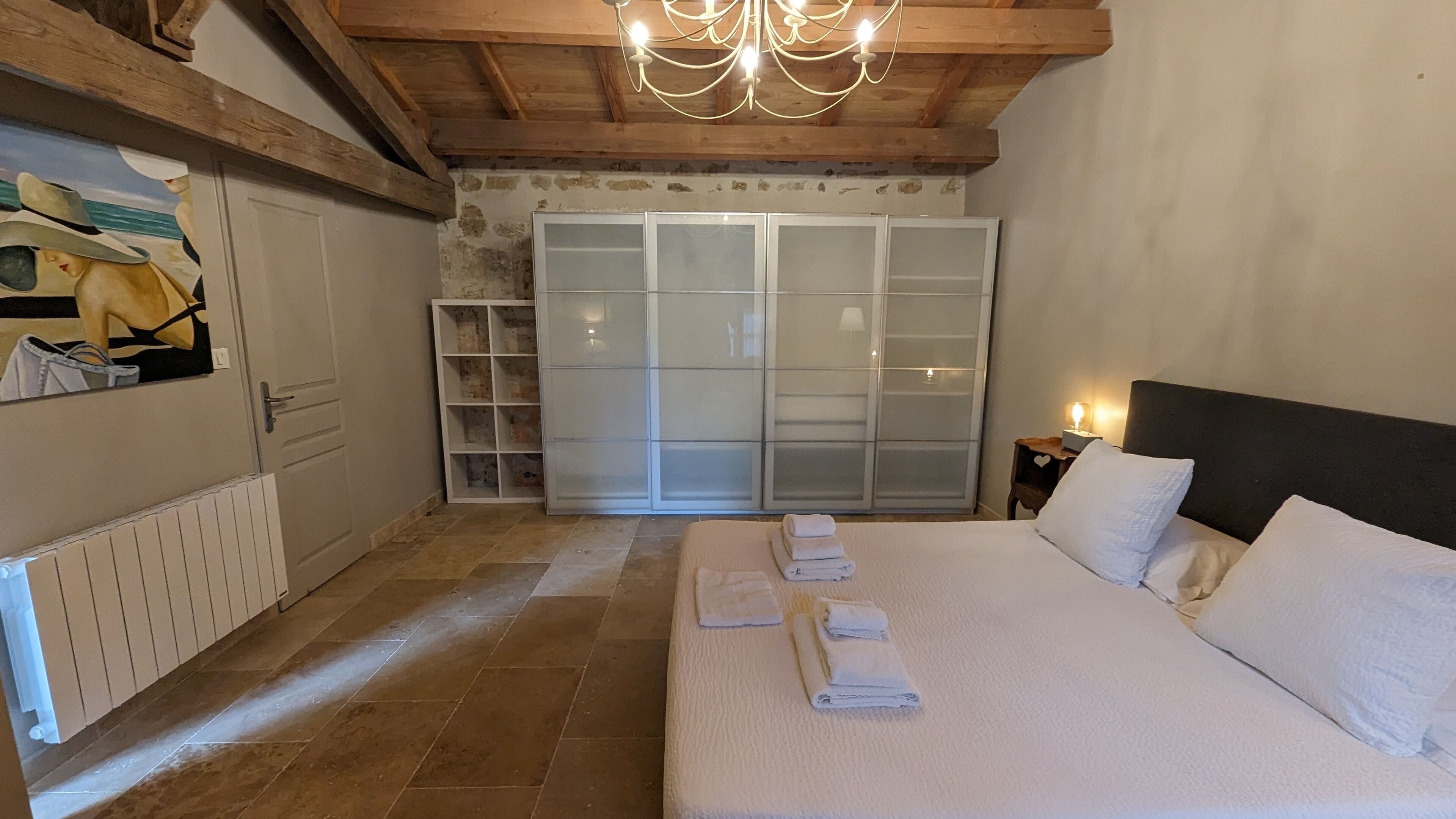 Een slaapkamer met een groot bed, een kledingkast, een radiator en een kroonluchter.