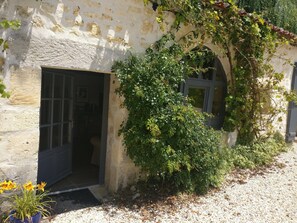 A rustic building with a door and a window, surrounded by greenery and a gravel path. - Montboulard (Soyaux)