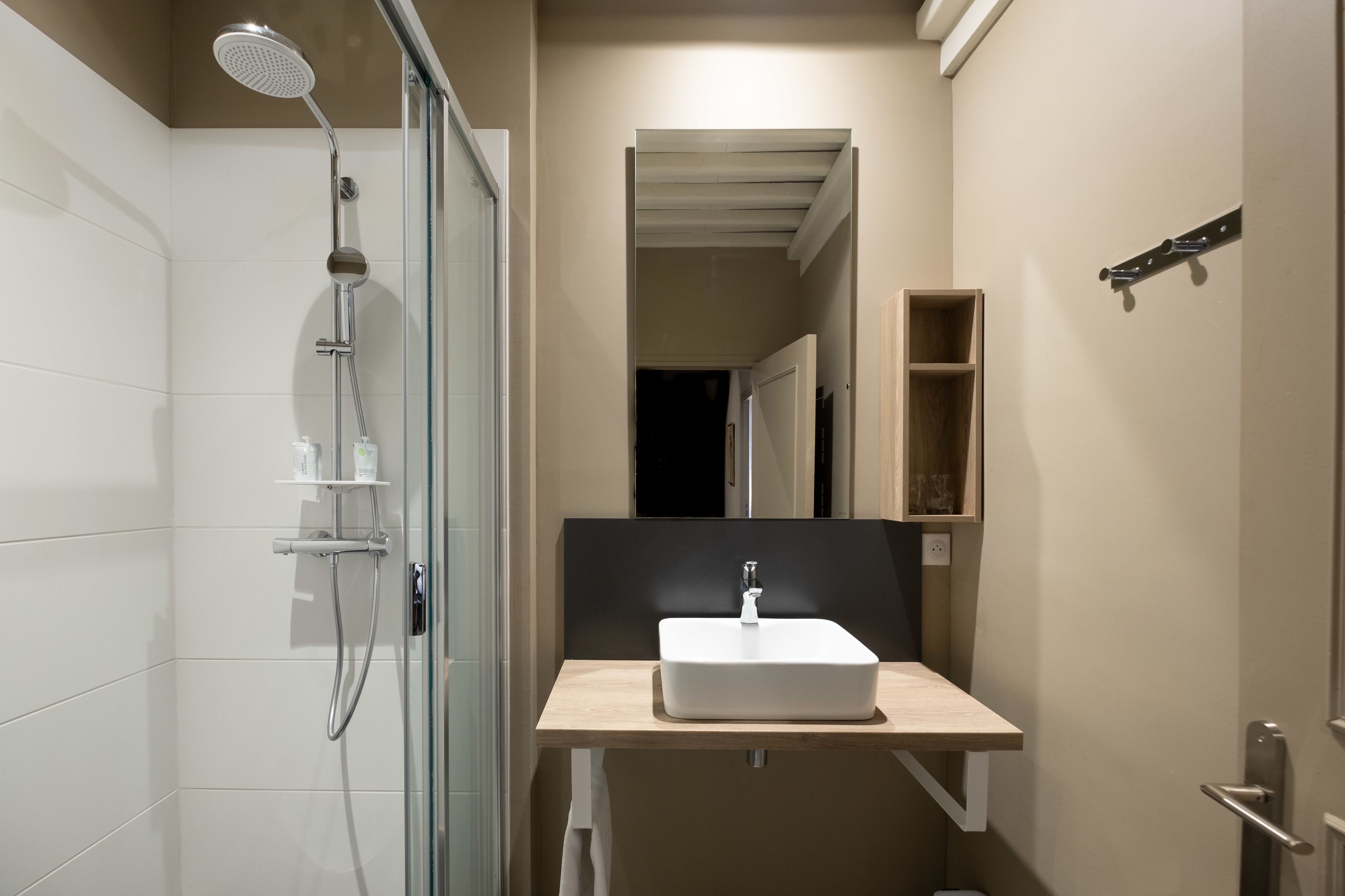 A modern bathroom with a glass shower enclosure, a white sink with a wooden countertop, and a mirror above the sink.