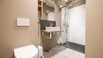 Un baño moderno con inodoro, lavamanos y cabina de ducha de vidrio.