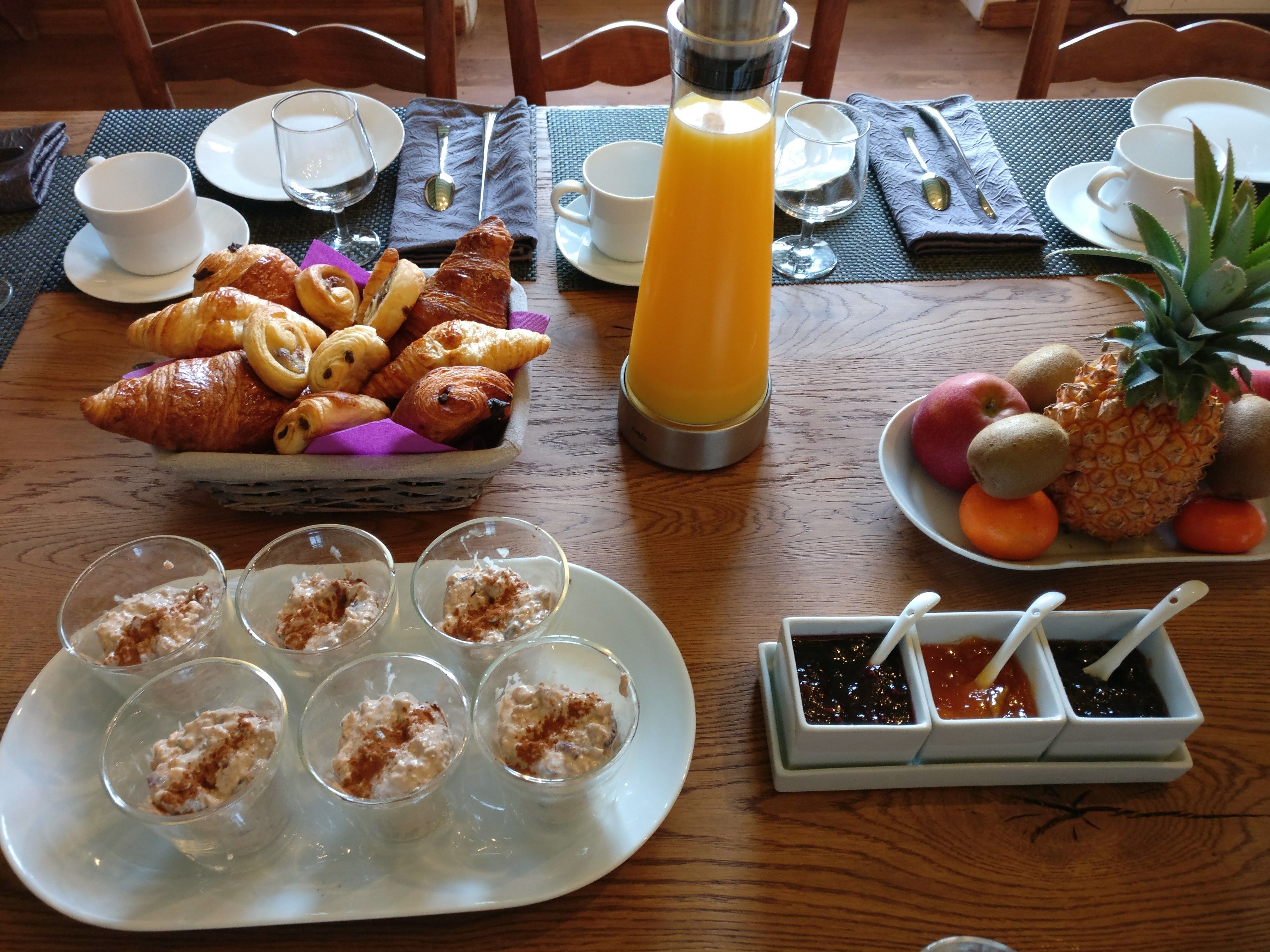 Colazione con croissant, frutta e bevande su un tavolo di legno.