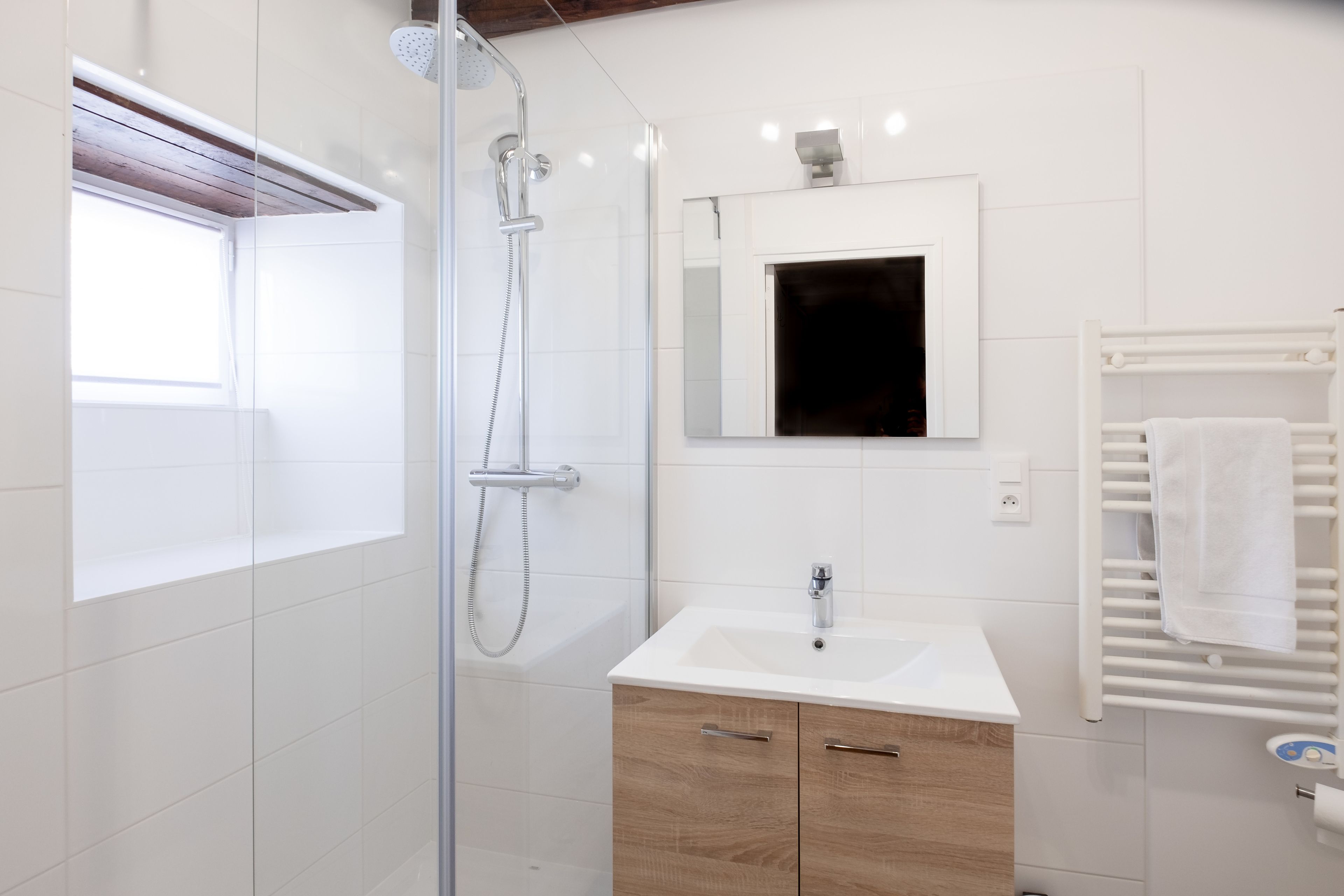 A modern bathroom with a glass-enclosed shower, a white sink, and a wooden cabinet.