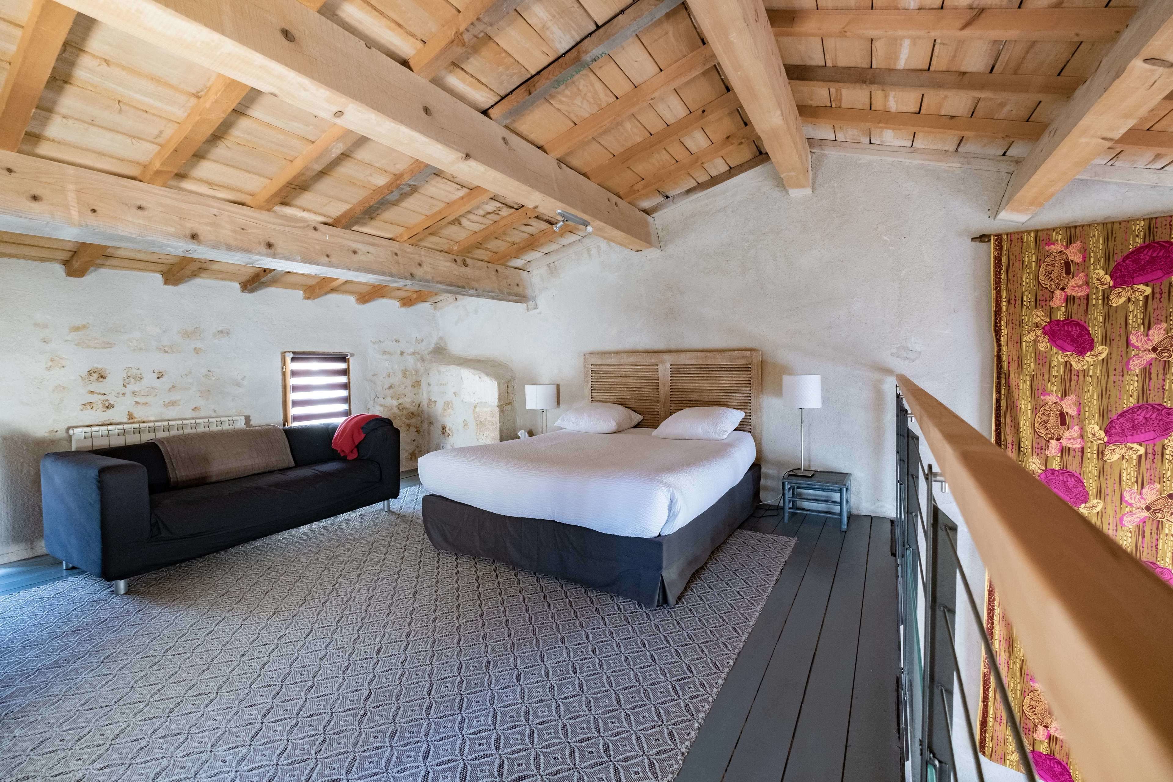 A bedroom with a bed, a sofa, a window, and a wooden ceiling.