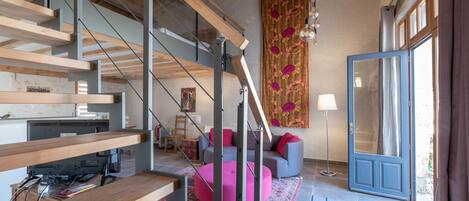 Um interior moderno com escada de madeira, um banquinho rosa e uma janela grande com cortinas.