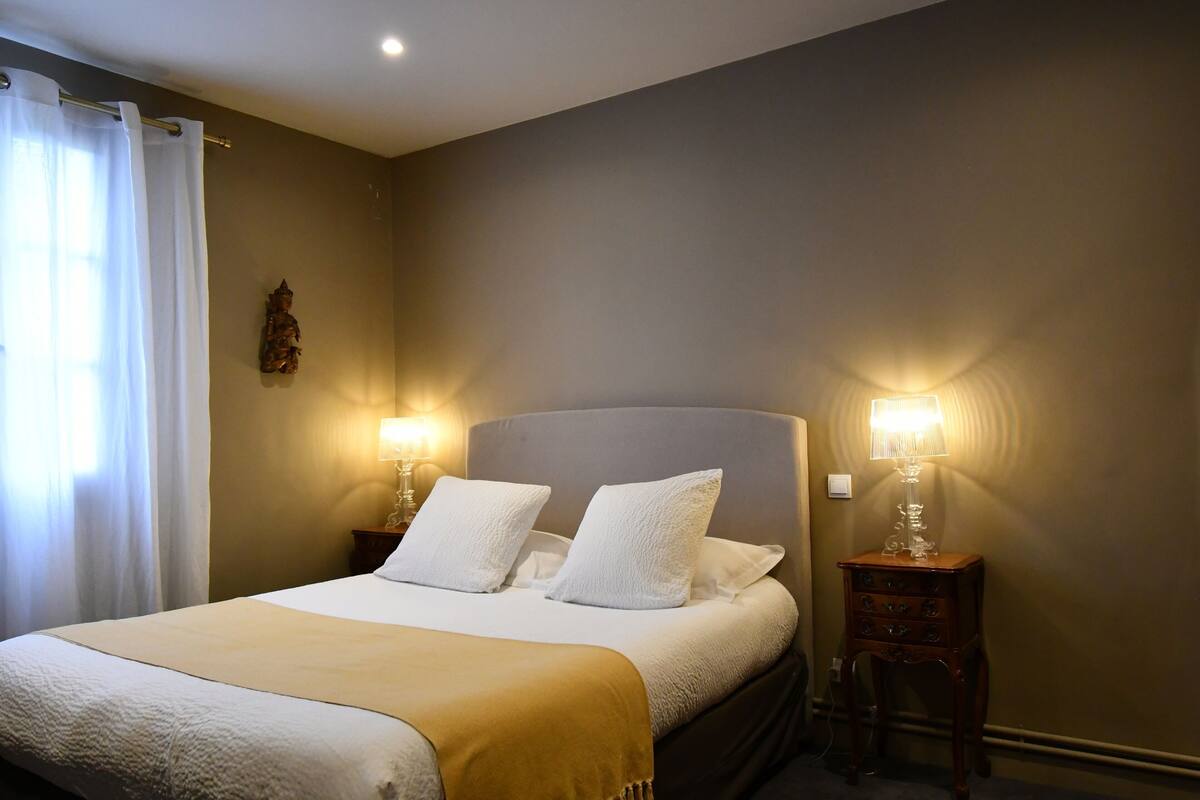 A neatly made bed with two pillows, a bedside table with a lamp, and a wall-mounted decoration.