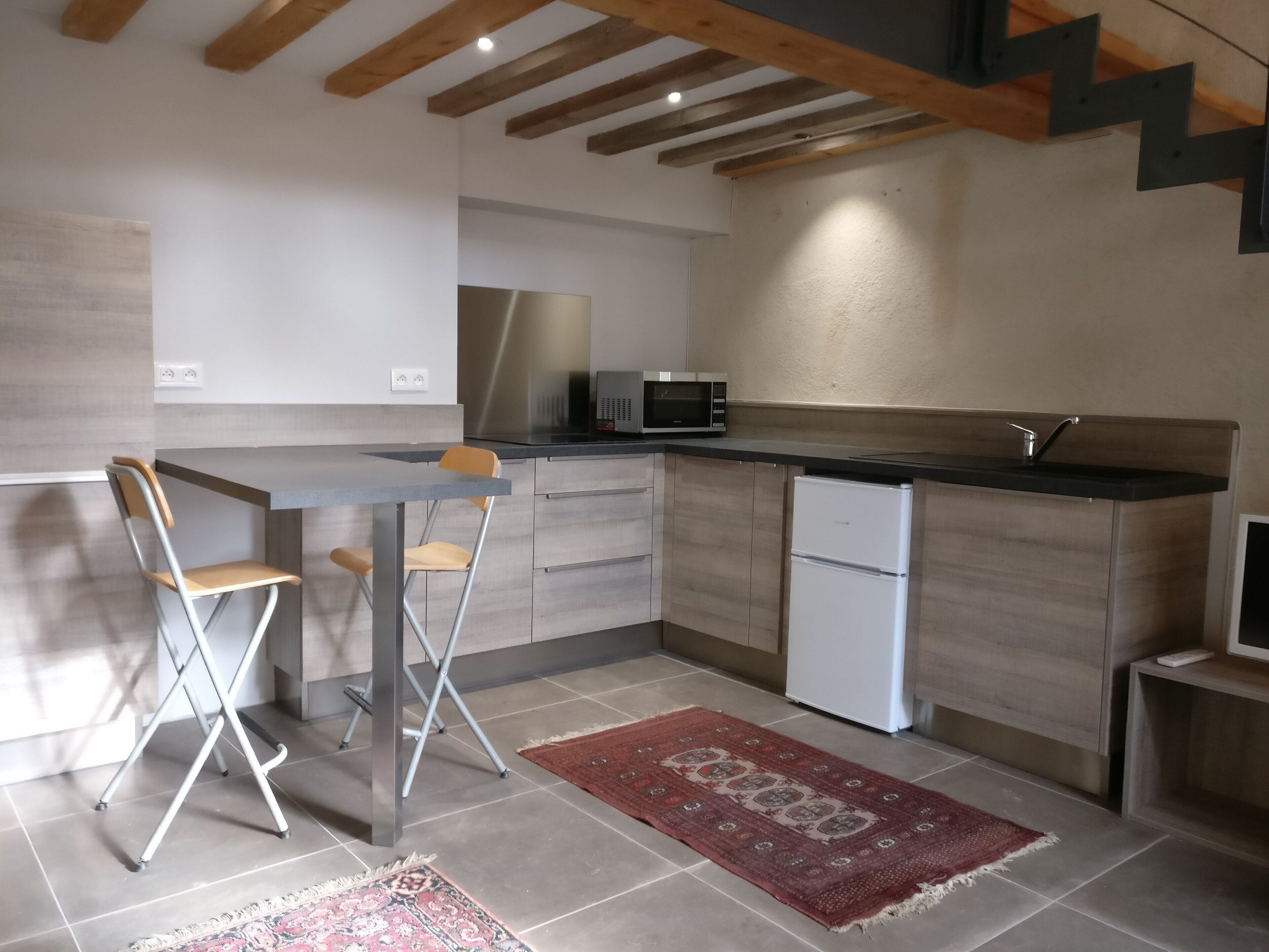 A modern kitchen with a built-in microwave, a refrigerator, and a sink. There are two foldable chairs and a patterned rug on the floor.