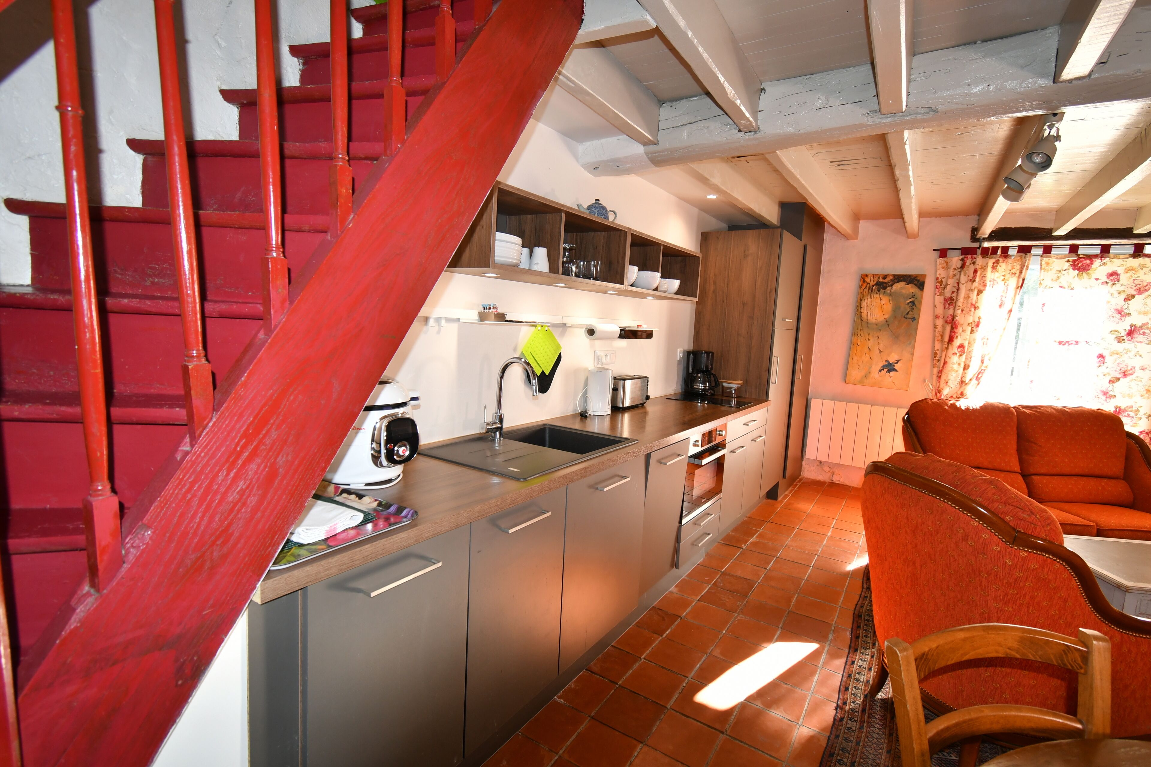 A kitchen with a red staircase, stainless steel appliances, and a wooden dining area.