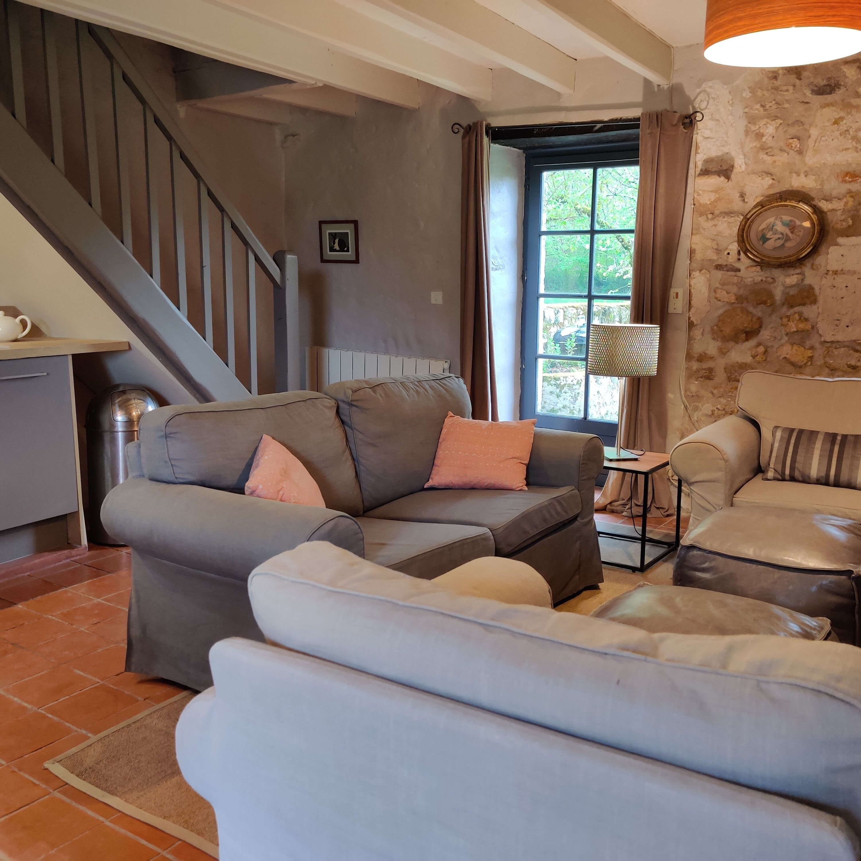 A living room with a grey sofa, a white sofa, a small table, and a lamp. There is a staircase in the background.