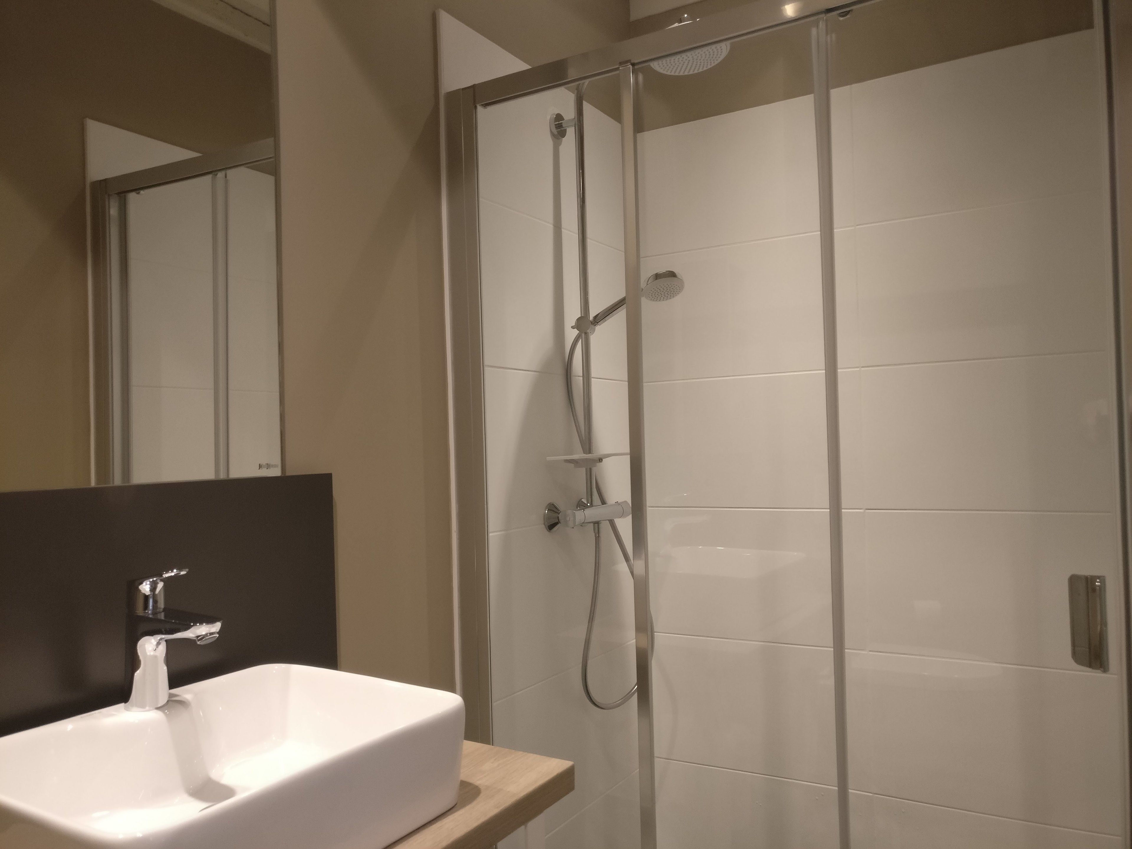 A modern bathroom with a glass-enclosed shower, a white sink, and a large mirror.