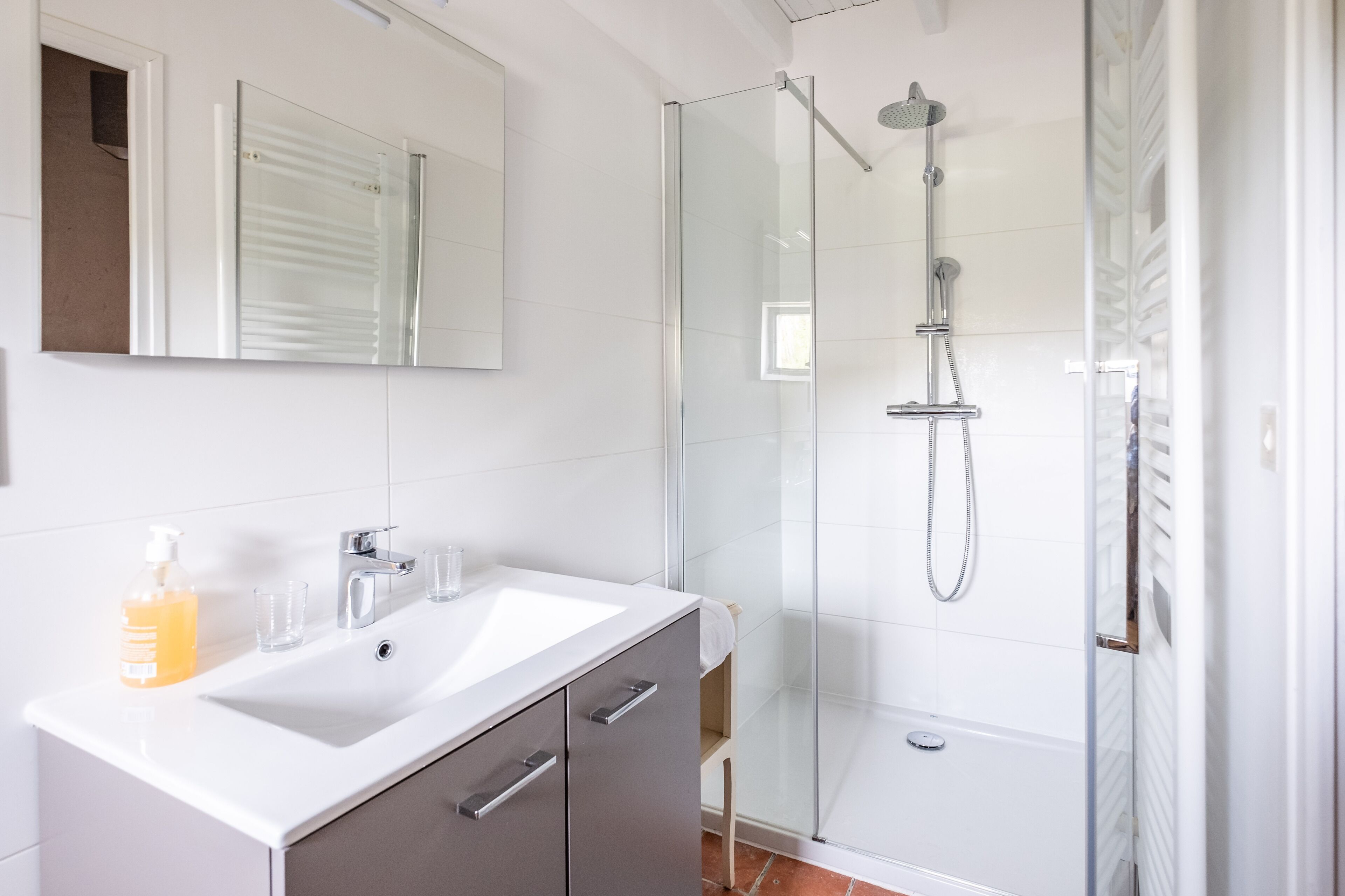 Un baño moderno con ducha de vidrio, un lavamanos blanco y un espejo sobre él.